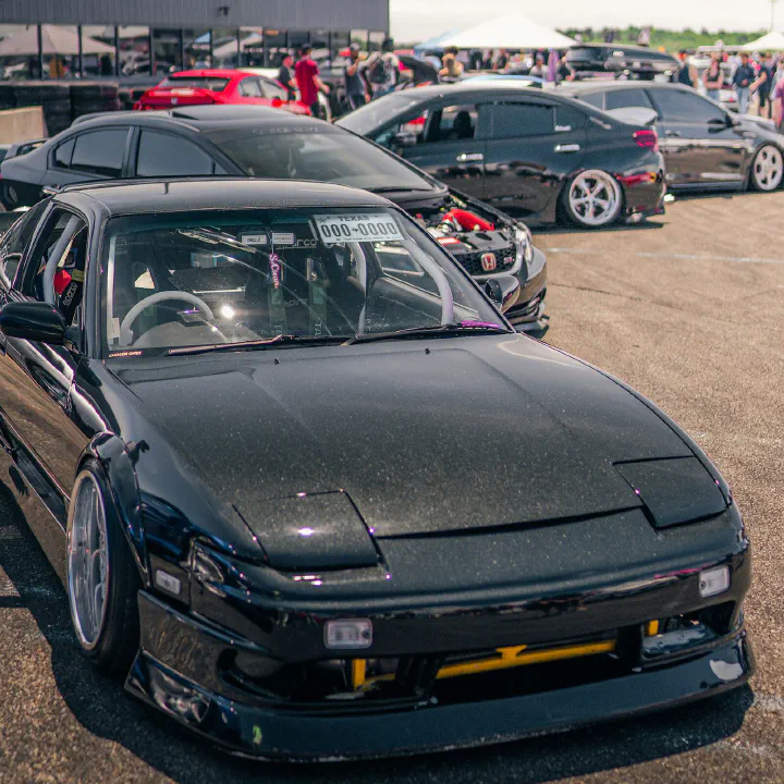 A black Nissan 240SX at a car meet, plate on the visor.