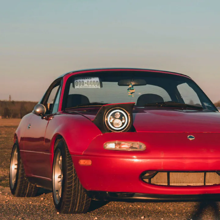 A red NA Miata at sunset with a plate on the passenger visor.